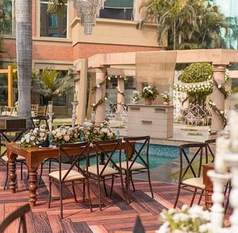 A beautifully decorated outdoor event space at Nirvana Luxury Hotel, Ludhiana, features elegantly set tables with floral arrangements beside a sparkling pool and lush greenery.