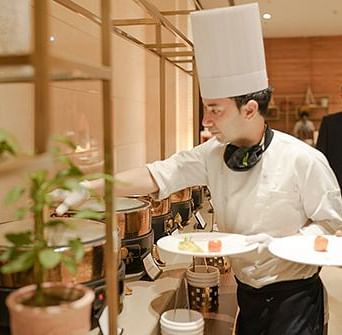 A chef grabbing food from a buffet while holding two dishes at Nirvana Luxury Hotel, Ludhiana.