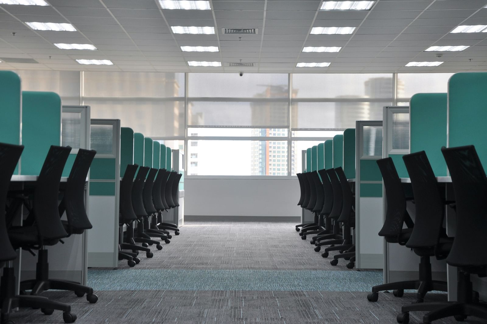 An empty office with rows of cubicles, chairs neatly arranged, and bright overhead lighting. 
