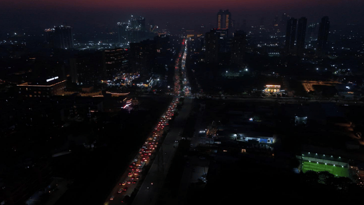 Night view of Gurgaon skyline with a long stretch of traffic-lit highway, high-rise buildings, and city lights glowing under a dark sky.