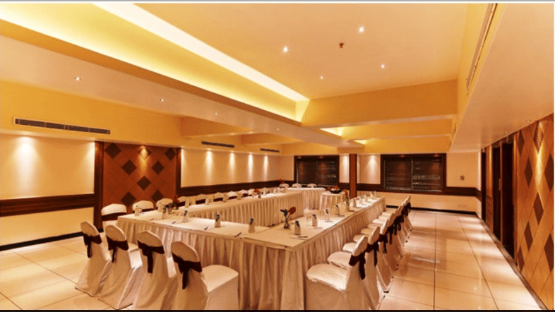 Banquet hall with arranged tables and chairs, ceiling lights, and wooden wall panels.