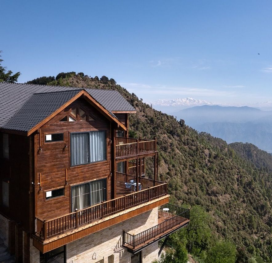 A view of a cottage and the balcony with a backdrop of mountains and clouds | Avalon Cottages, Kanatal