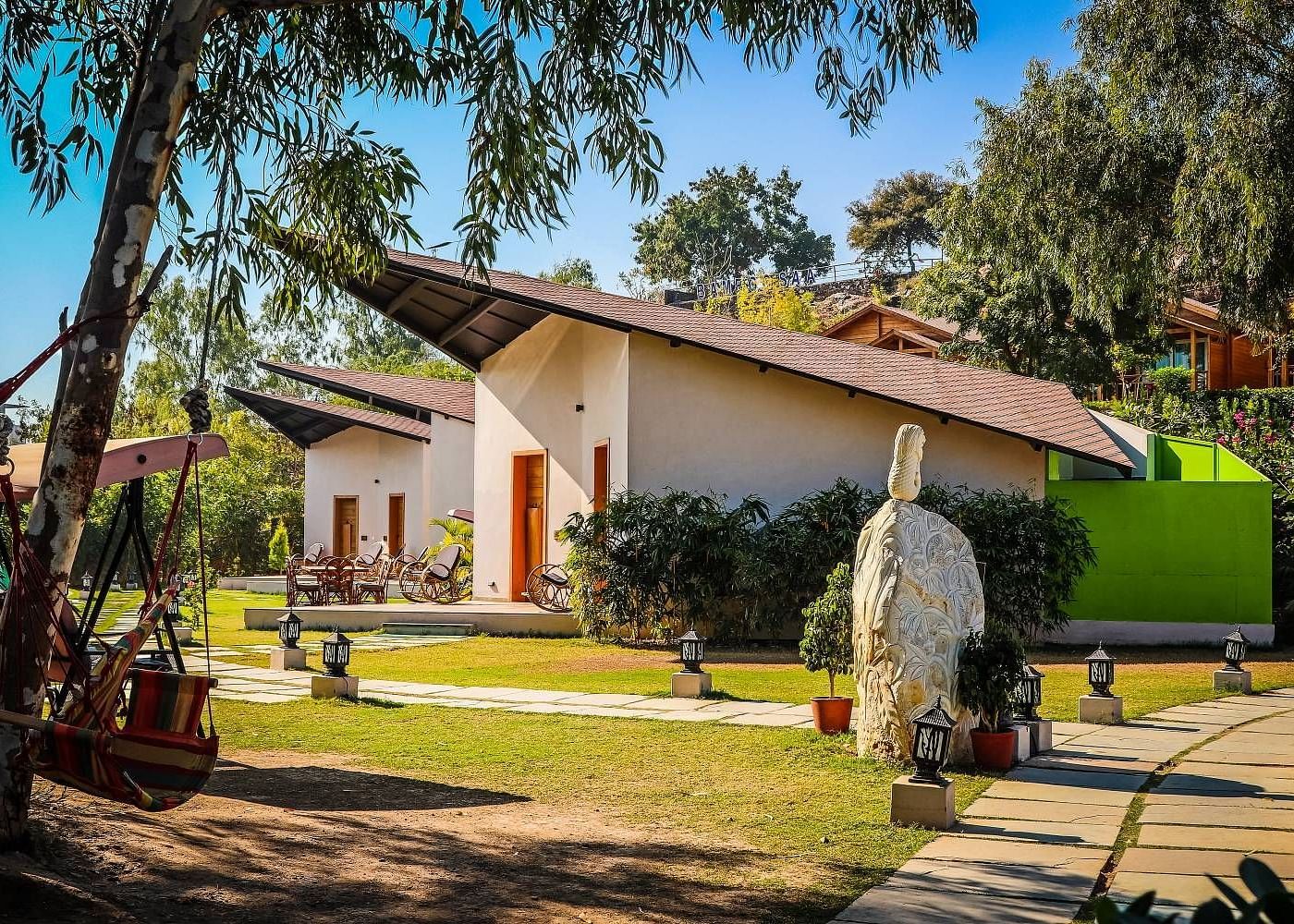 A modern building with a sloping roof sits amidst lush greenery.- Bamboo Saa Resort & Spa, Udaipur