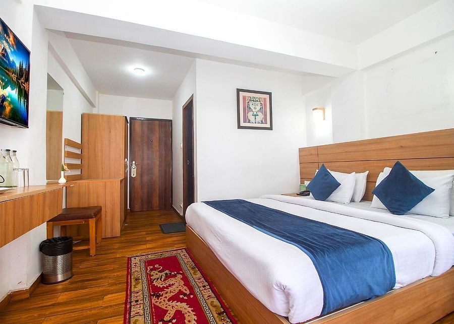A room with double bed, Framed art work on the wall, TV, Wardrobe, Dustbin, Table and desk with two water bottles on the top at  Central Heritage Resort and Spa (Formerly Fortune ITC Resort) The Mall Road.