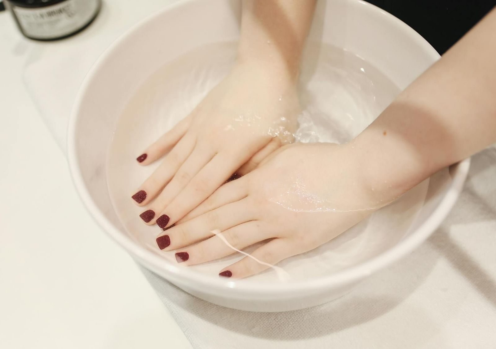 A bowl filled with water with two hands placed inside, showing neatly manicured nails