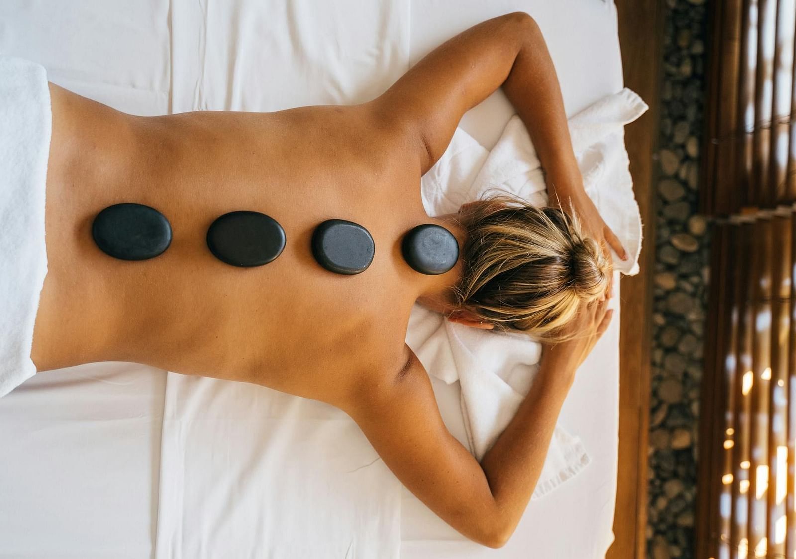 An image of a lady lying face down with her hands positioned in front forming a triangle, and lava stones placed along her back