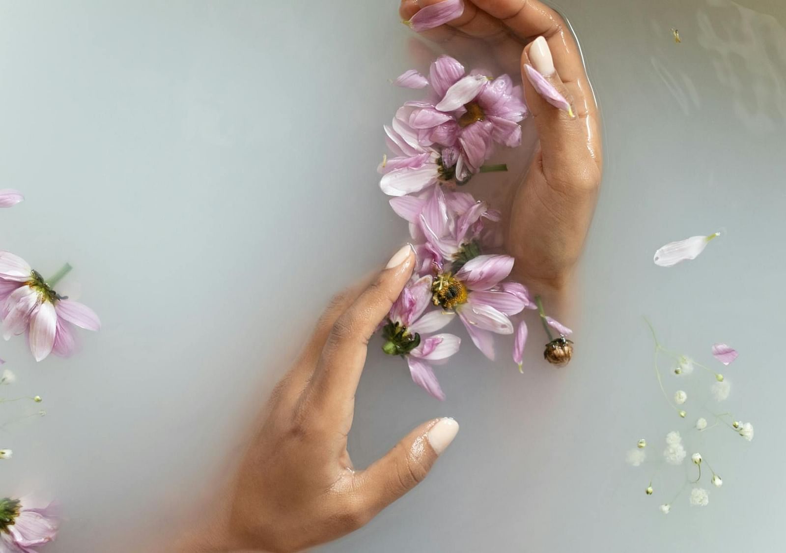 Milky water with a person’s hand submerged, holding flowers that float on the surface