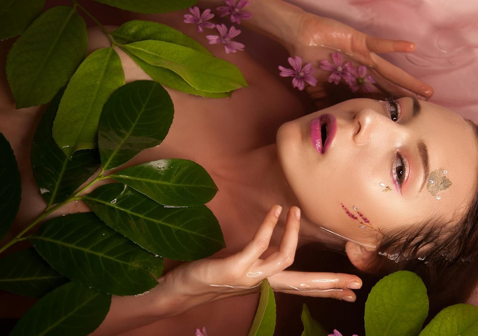 A lady in the water with her hands on her face, surrounded by floating leaves and flowers