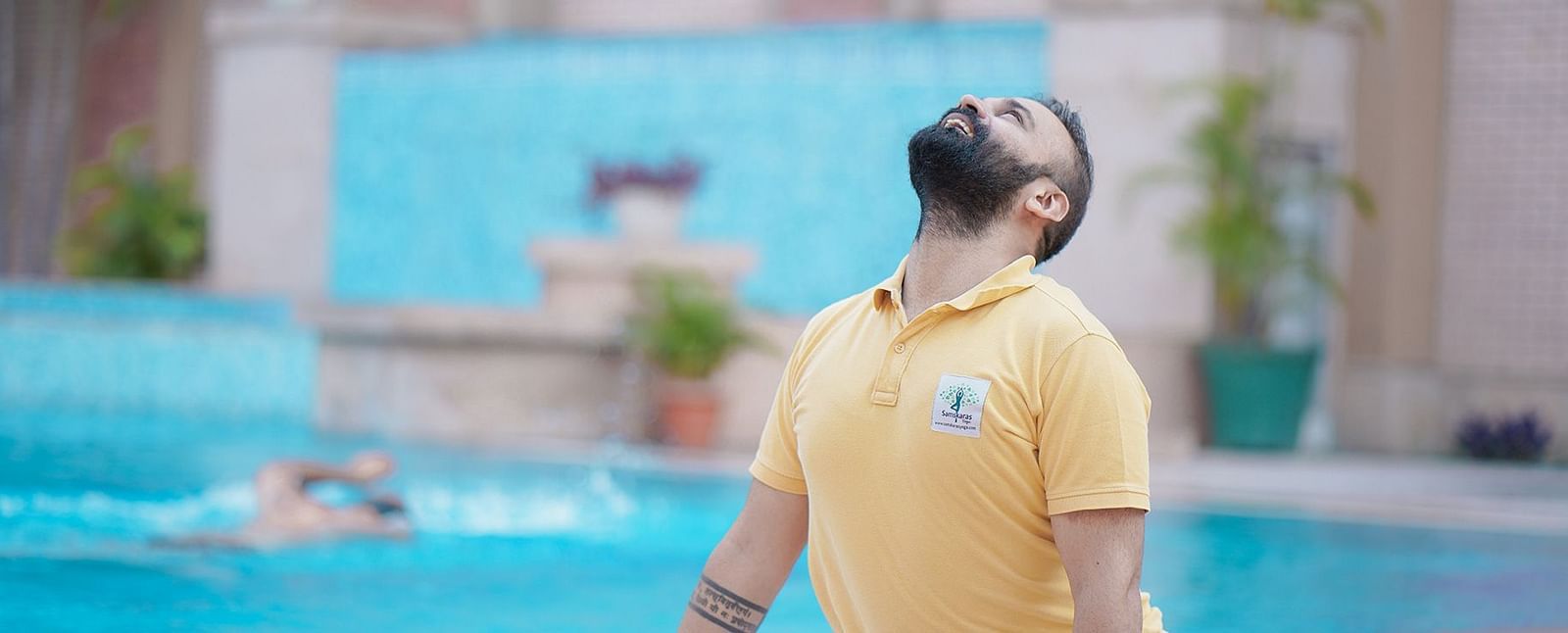 A man practising yoga with a swimmer in the background at Nirvana Luxury Hotel, Ludhiana.