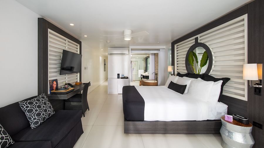 An image of a hotel room with warm night lamps, a wall-mounted television and a black couch - S Hotel Montego Bay, Jamaica