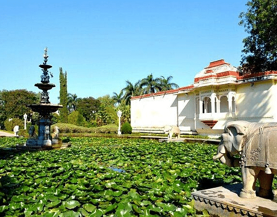 A pond filled with lily pads and a fountain in the background. 