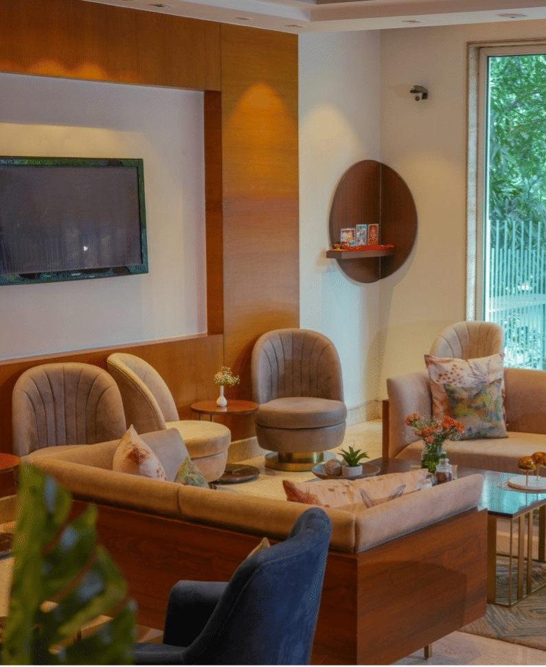 Warm and stylish lounge area with plush seating, TV, and large window views at Hotel Saket 27, New Delhi.