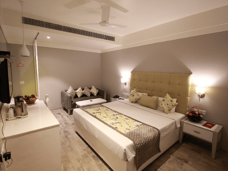 Elegant room with a large bed, bed side table, sofa, and TV unit at Hotel Emerald, Chandigarh