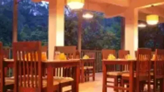 A spacious dining room features numerous wooden tables and chairs, illuminated by soft, warm lighting. - Abad Brookside Lakkidi, Wayanad