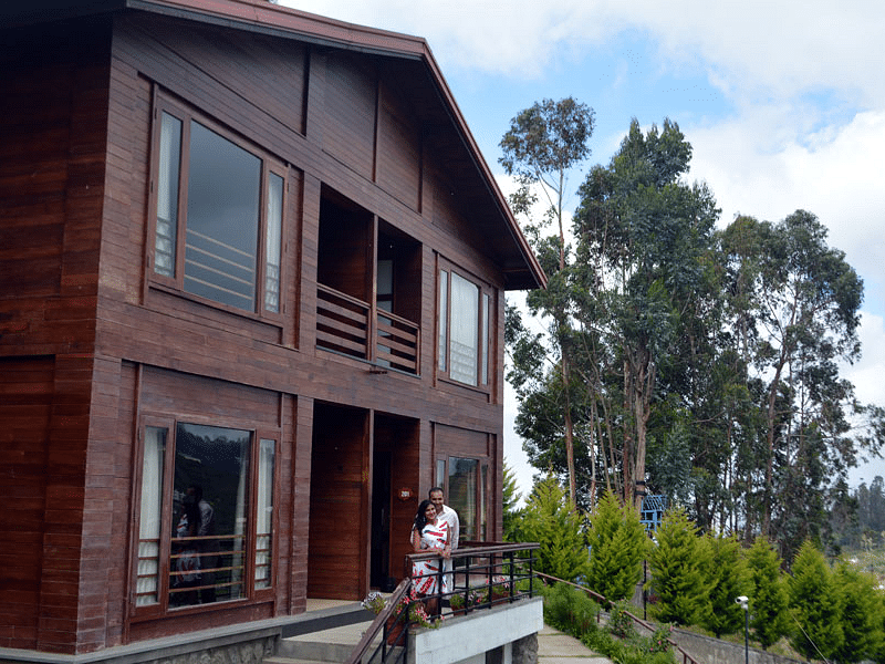 Modern wooden villa surrounded by greenery and an outdoor seating area.