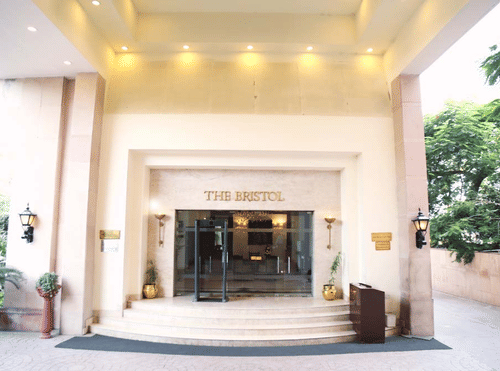 The entry door of The Bristol Hotel features an extended portico that offers overhead lighting to the entry of the best hotel in Gurgaon for corporate outing.