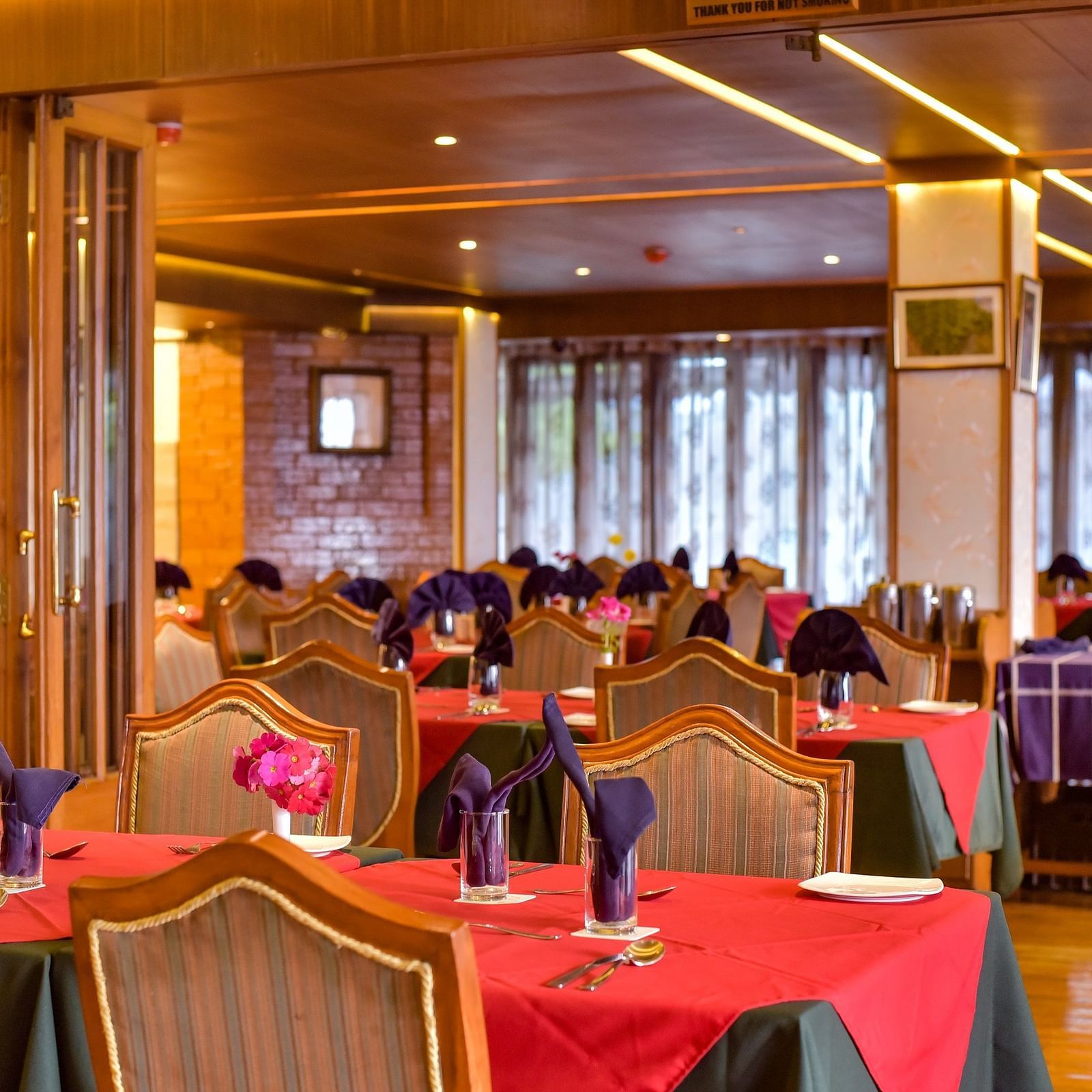 Dining area at Cedar Inn, Darjeeling, featuring elegant wooden interiors, red and green tablecloths, and neatly folded napkins on each table.