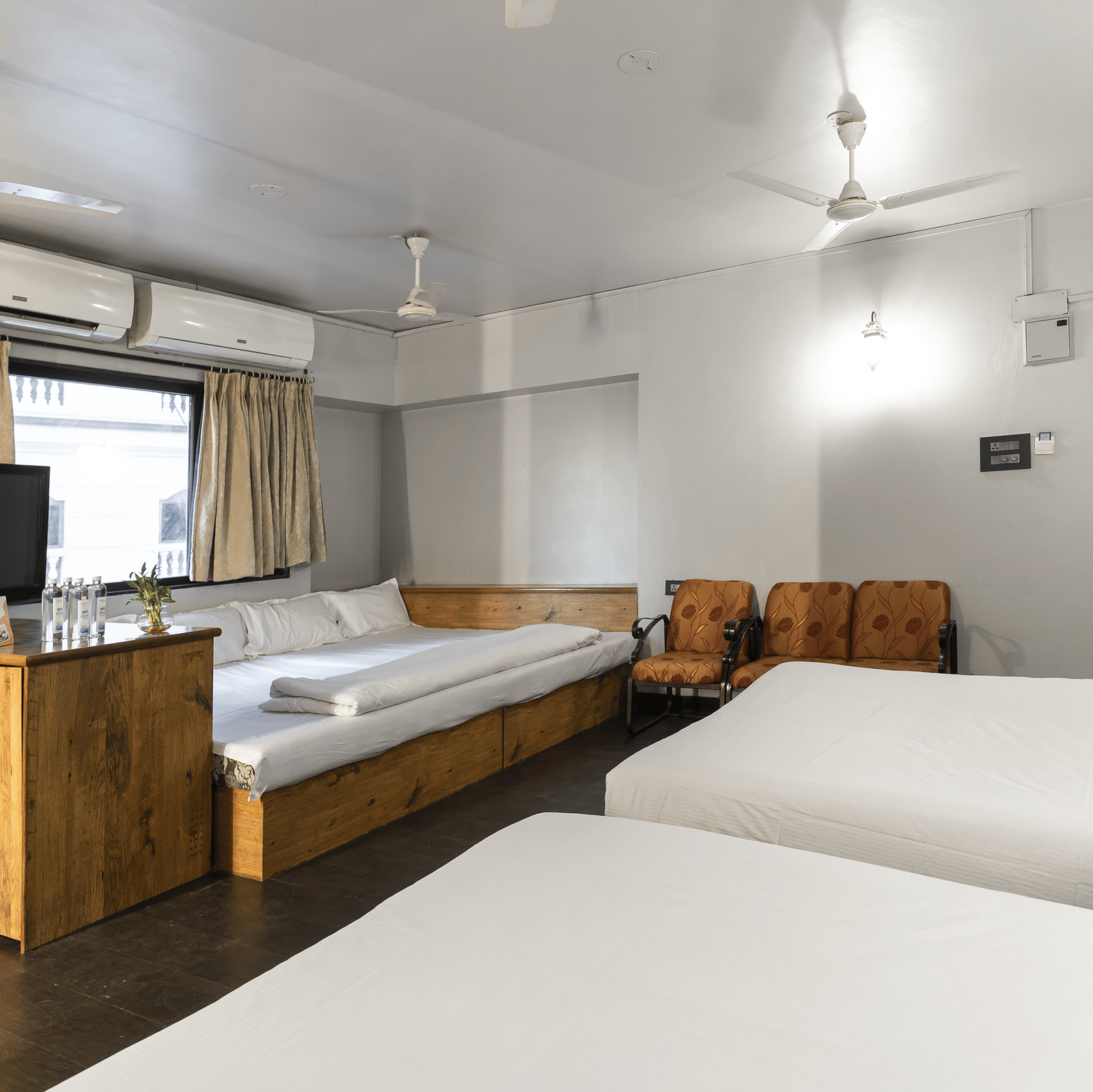A room with multiple beds, wooden furniture and a television at Infiniti Hotel, Indore.
