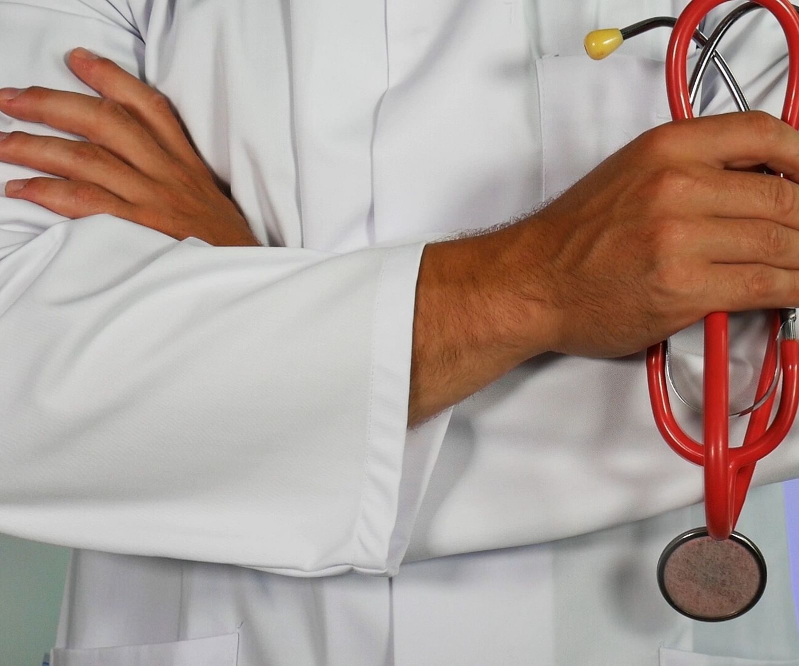 a close up image of a doctor with folded hands hoding a stethoscope 