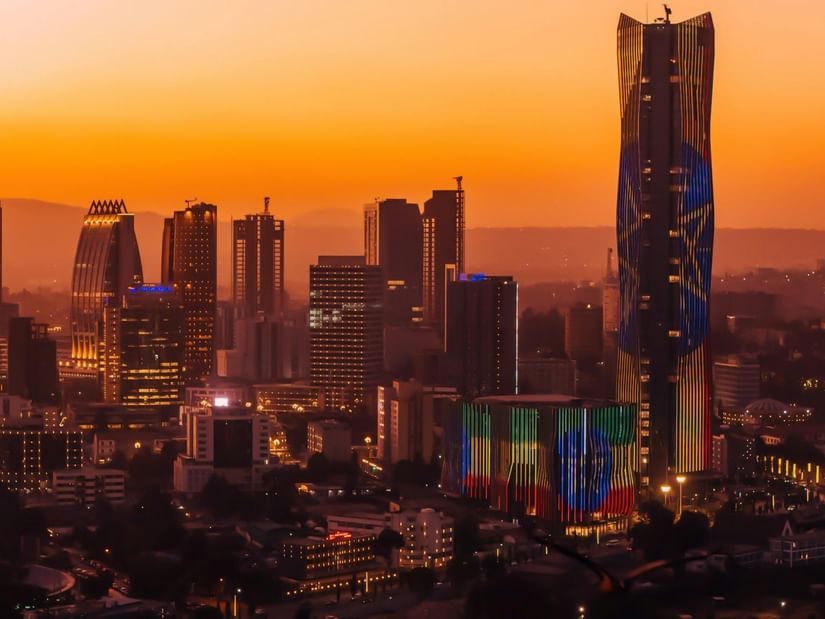 City skyline at sunset, featuring modern skyscrapers and a prominent glass tower.