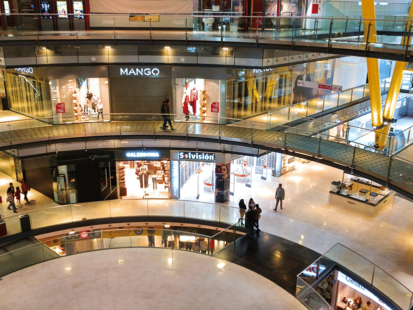A view from the top floor of the interior of a mall with numerous shops lined up next to each other.