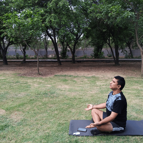 A visitor practises yoga on the grass in a peaceful park surrounded by trees.