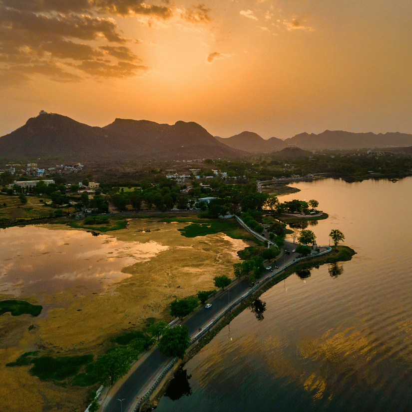 Aerial view of Fateh Sagar Lake at sunset with golden reflections on the water and hills surrounding the lake