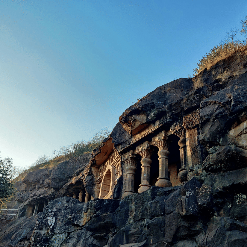 A view from below of one of the Pandavleni Caves (Nashik), a 3rd century BCE cave, on the side of a mountain with blue sky in the background.