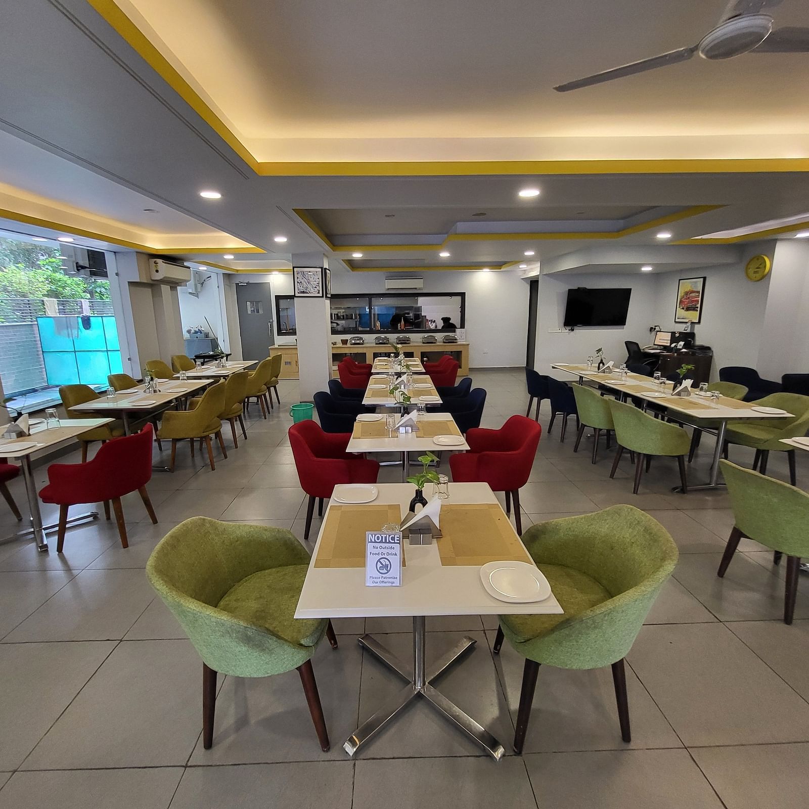 An image of a restaurant at Inde Hotel Golf Course Extension featuring several sets of chairs and tables where plates and table mats are placed