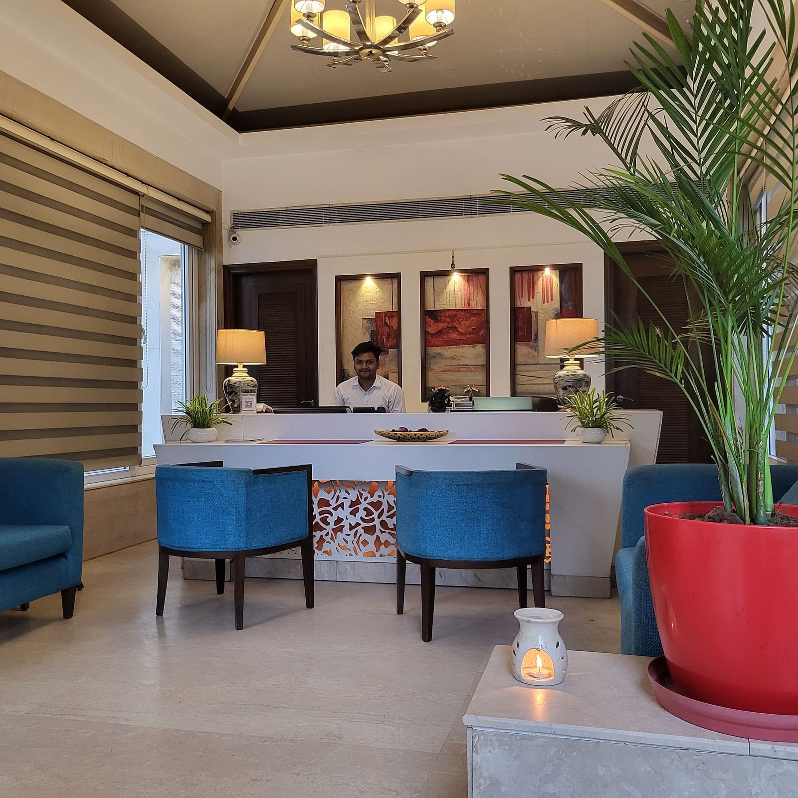 A reception lobby featuring sofas, chairs, reception desk where a receptionist is sitting, and lights hanging from the ceiling - Inde Hotel Signature Tower Gurgaon