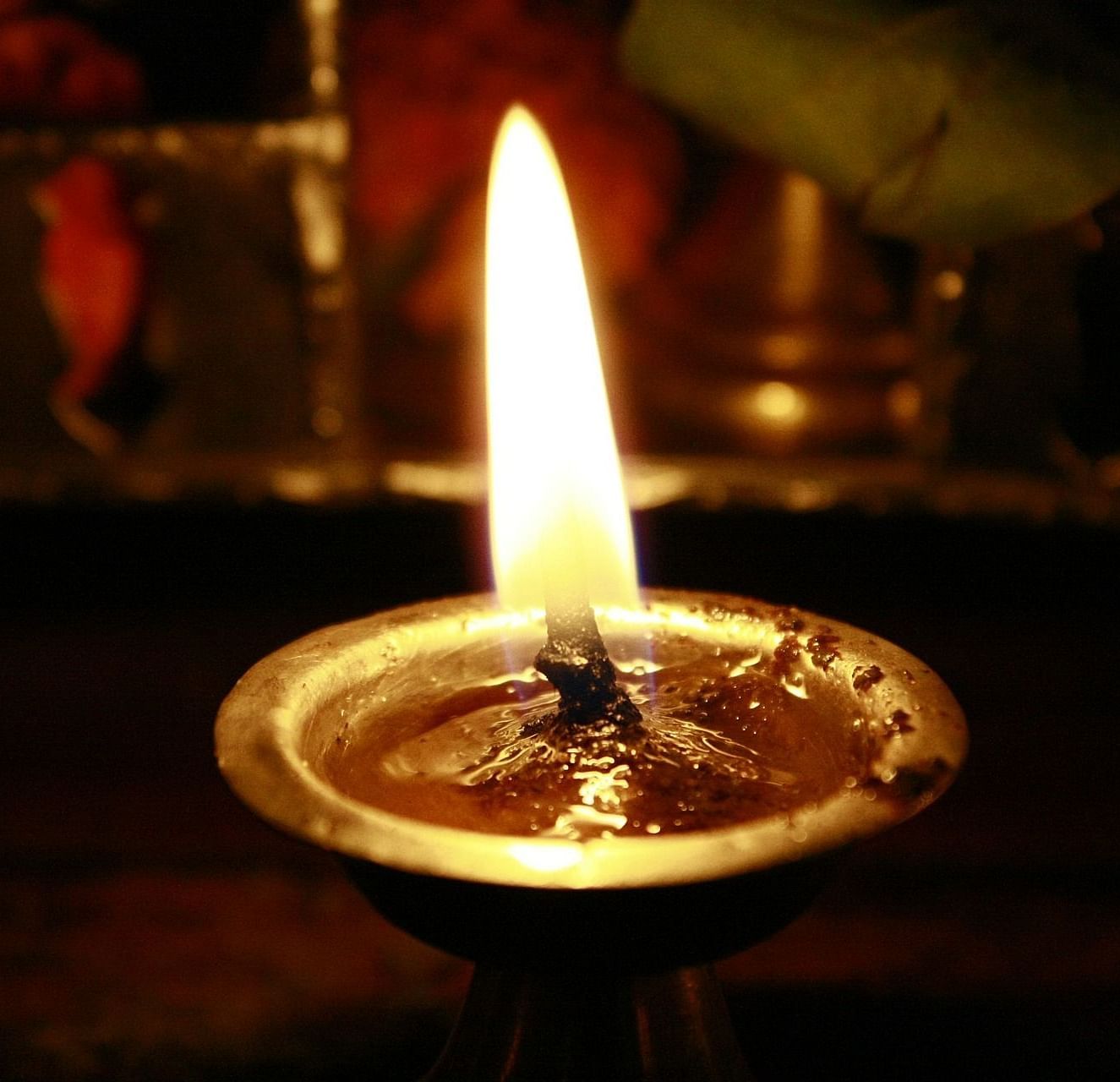 A lit oil lamp, the flame is bright and steady against a dark background.