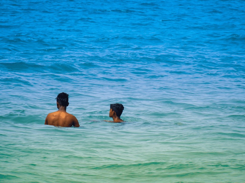 A zoomed in view of two people bathing in the Arabian Sea next to Colva Beach, one of the top 10 beaches in South Goa, in blue-green coloured waterbody.