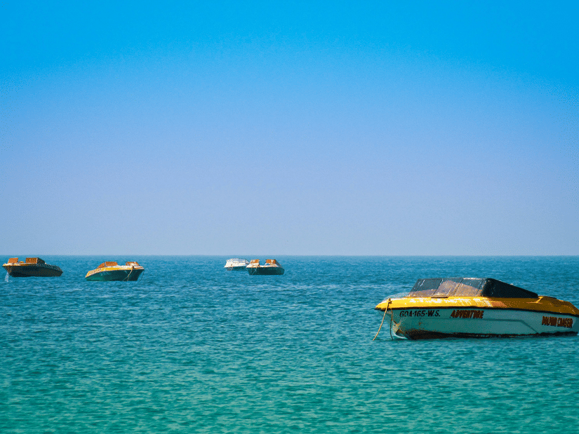 Numerous boats on the Arabian Sea next to Colva Beach with blue-green waterbody and blue sky seen.