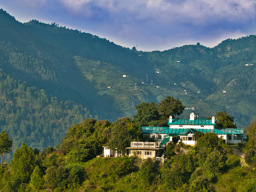 Facade of The Ramgarh Bungalows perched on a hill surrounded by scenic mountain view captured during the day.