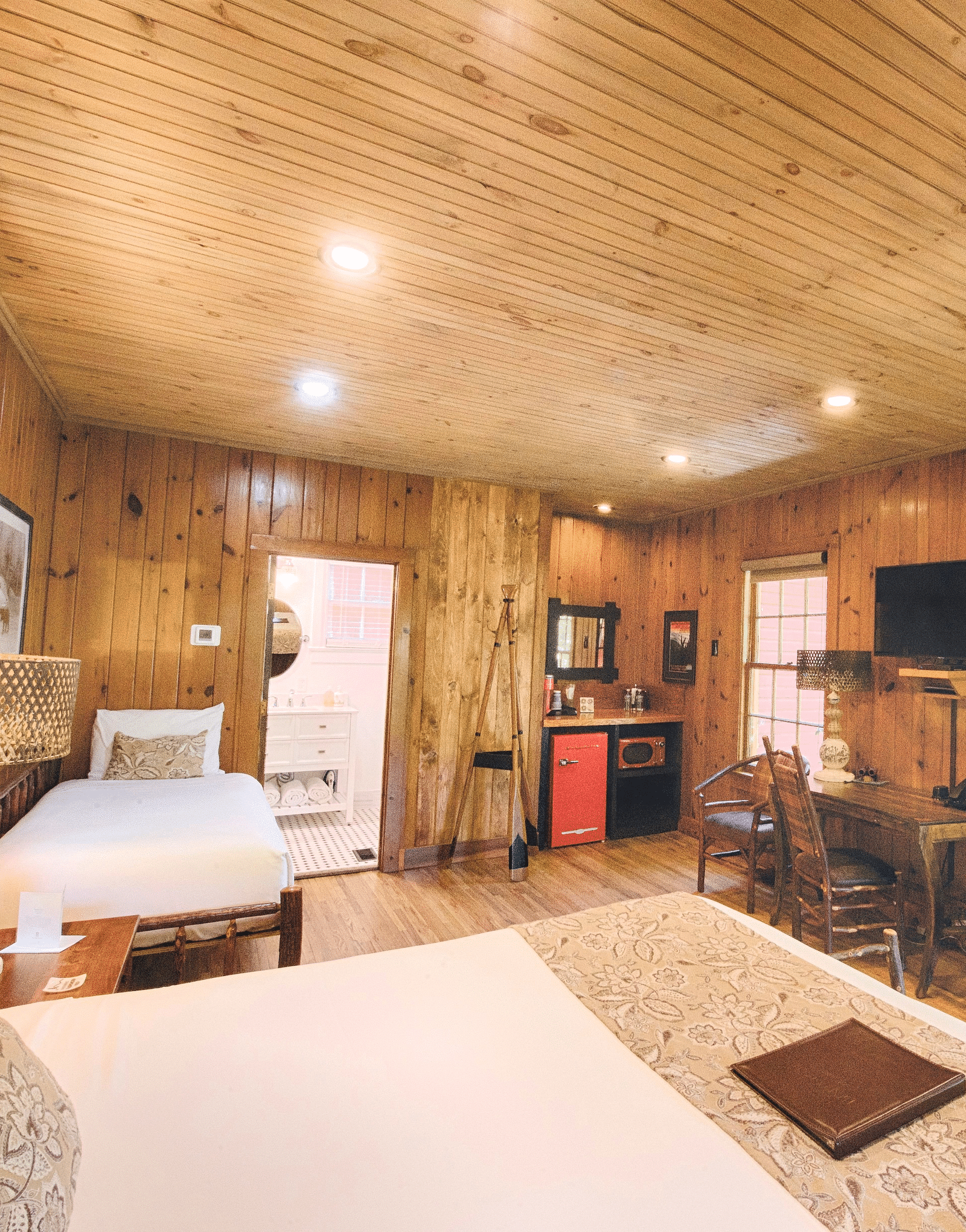 a bedroom overlooking a double bed with a file kept on it facing towards a window with lush green views outside - Historic Tapoco Lodge