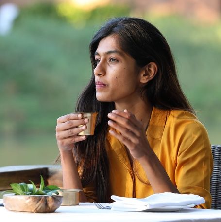 Woman in yellow holds a coffee Cup and looks outdoors.