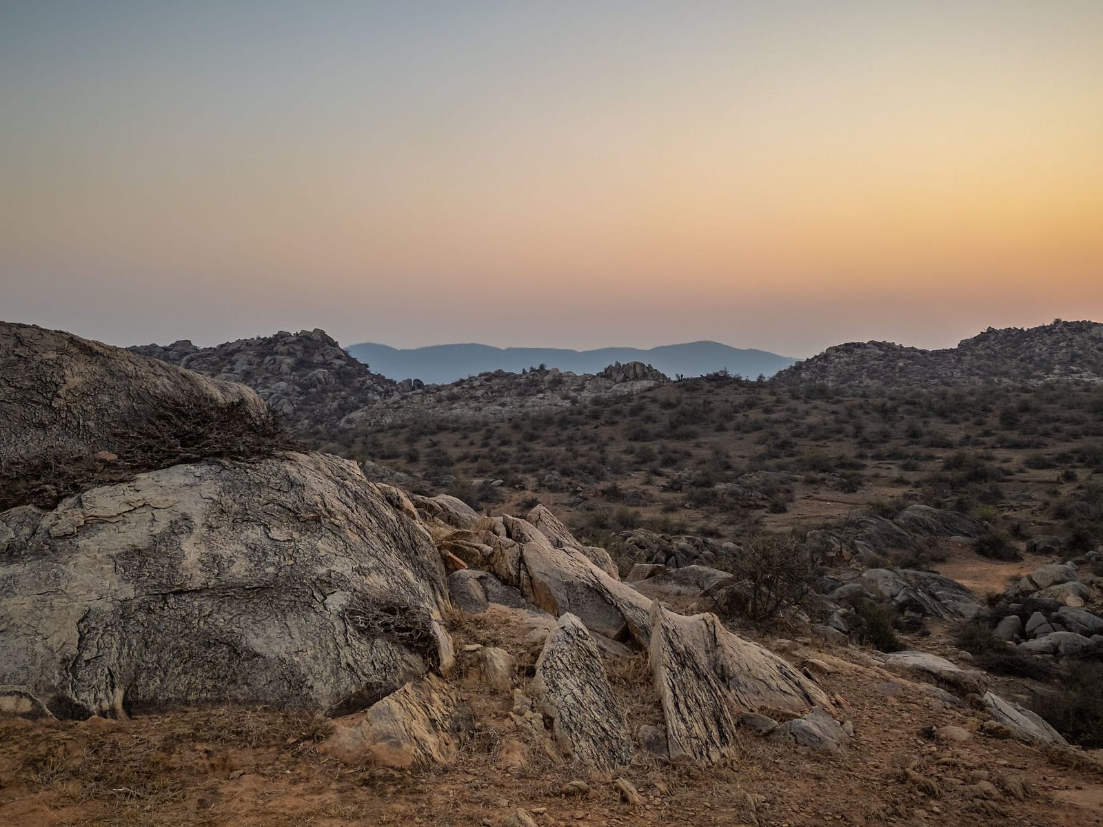 Overcast sunset view of a valley with rocky hills, golden light on the horizon.