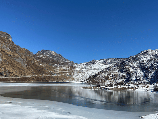 an image of Changu lake of sikkim captured during the day with crystal clean water and enveloped by mountains