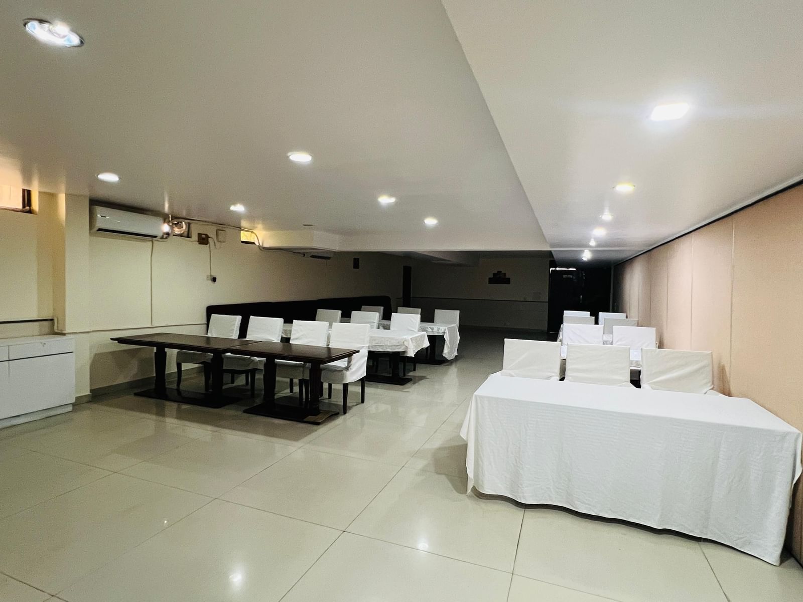  A hotel conference room with long tables and white chairs arranged for an event, featuring modern lighting and light-colored walls. | Hotel Aadhar