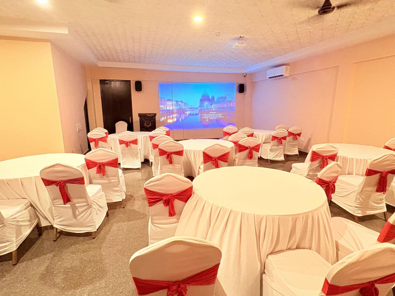 A well-lit conference hall with round tables and red chairs, ideal for meetings and events at Nazri The Verda, Arambol.