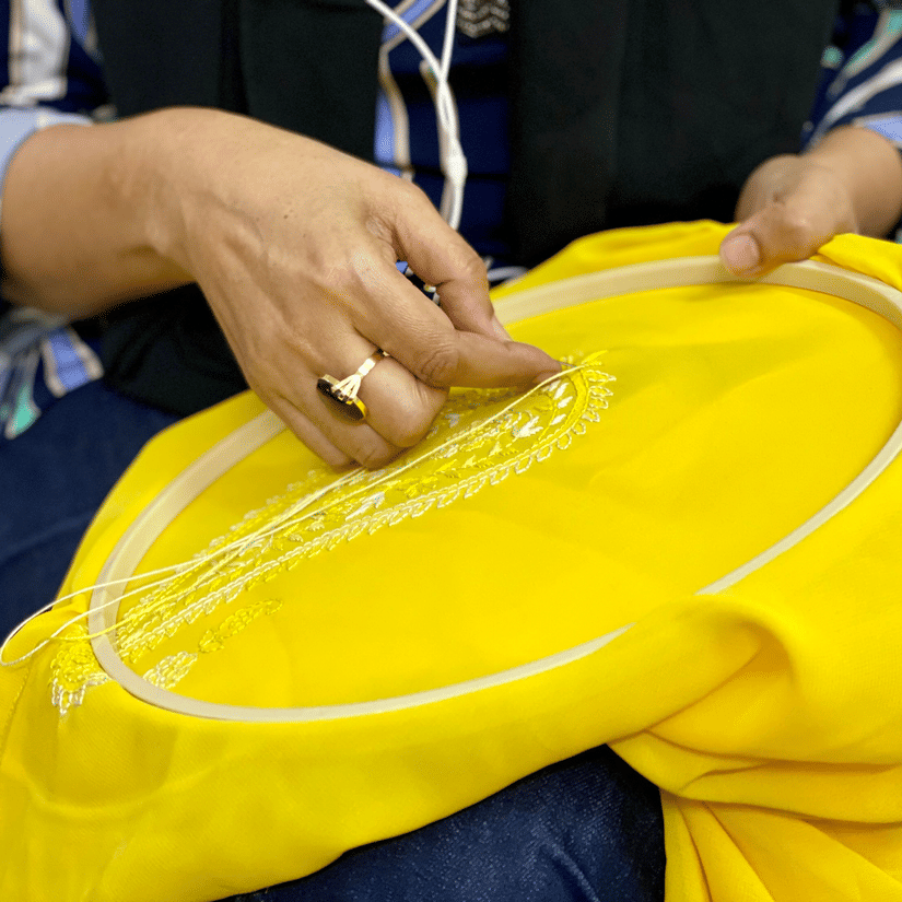 Close up of a woman weaving a peace of yellow-coloured cloth locked in an embroidery ring with thread and needle.