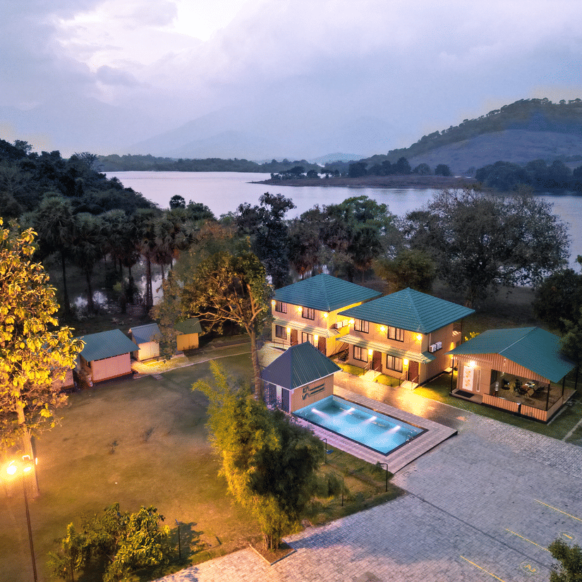 The illuminated facade of Ibex Resorts, Malampuzha (Kava Eco Camp and Caravan Park), featuring trees, and greenery in the evening