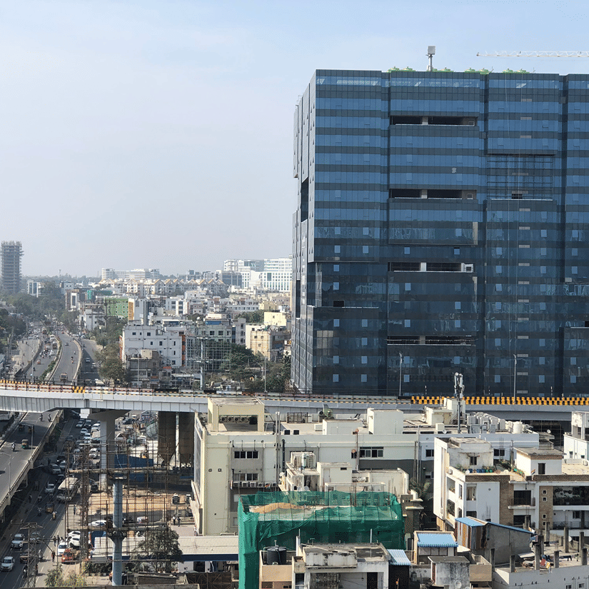 An aerial view displays a dark glass high-rise standing above a sprawling cityscape with a major busy flyover below.
