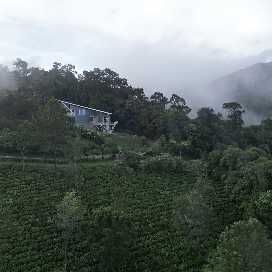Aerial view of a triangular-roofed house surrounded by dense forest canopy at Ibex Resorts, Coonoor (Tapas).