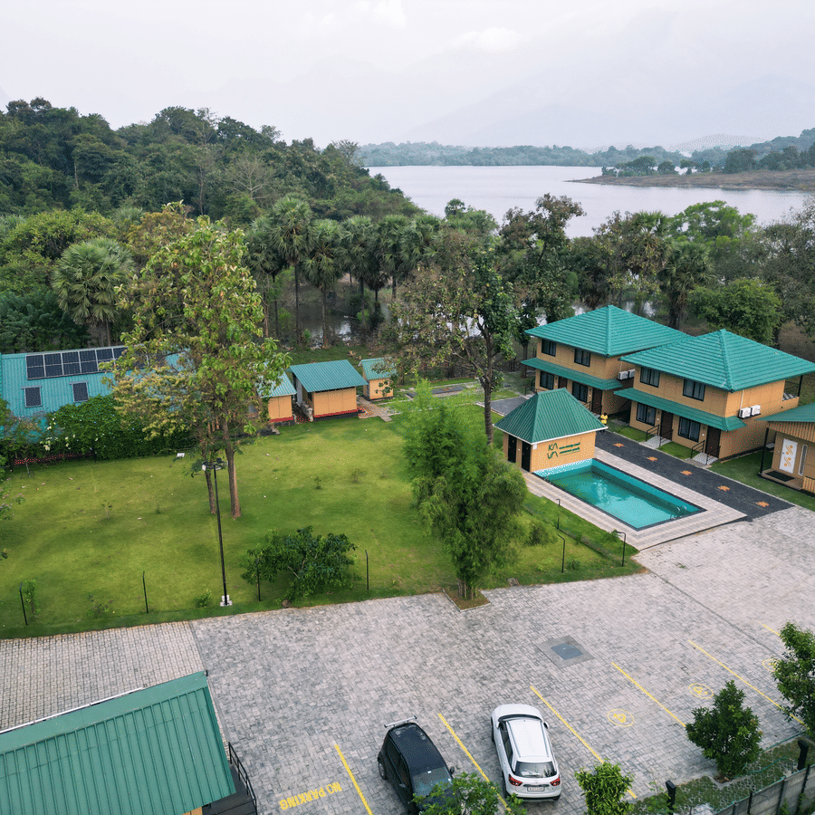 The facade of Ibex Resorts, Malampuzha (Kava Eco Camp and Caravan Park), featuring trees, and greenery in the morning.