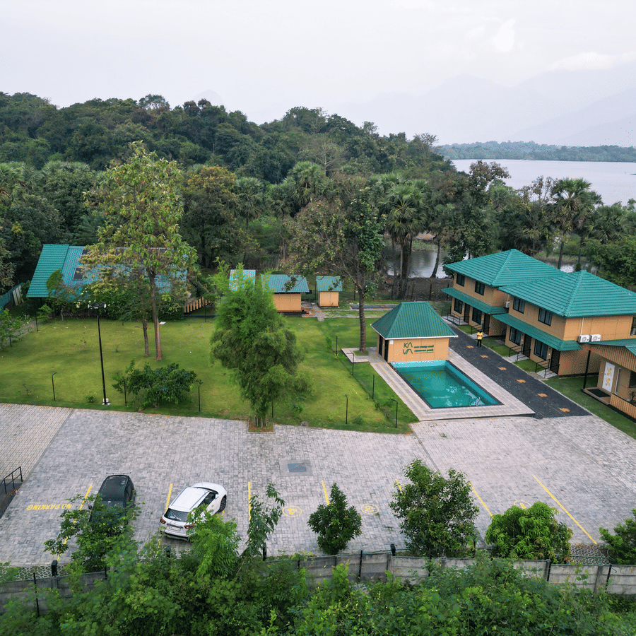 The illuminated facade of Ibex Resorts, Malampuzha (Kava Eco Camp and Caravan Park), featuring trees, greenery, and a pathway.
