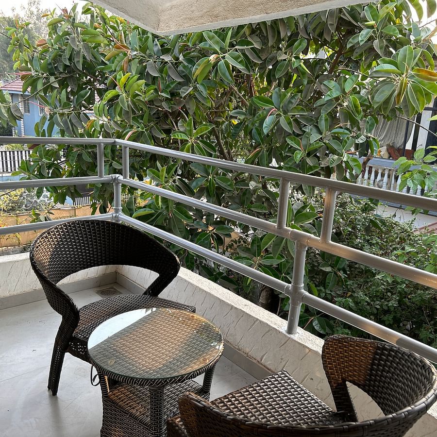 A serene private balcony with stylish wicker chairs and a glass-top table, surrounded by lush greenery– Maxxvalue Klub Klass Villa, Lonavala.
