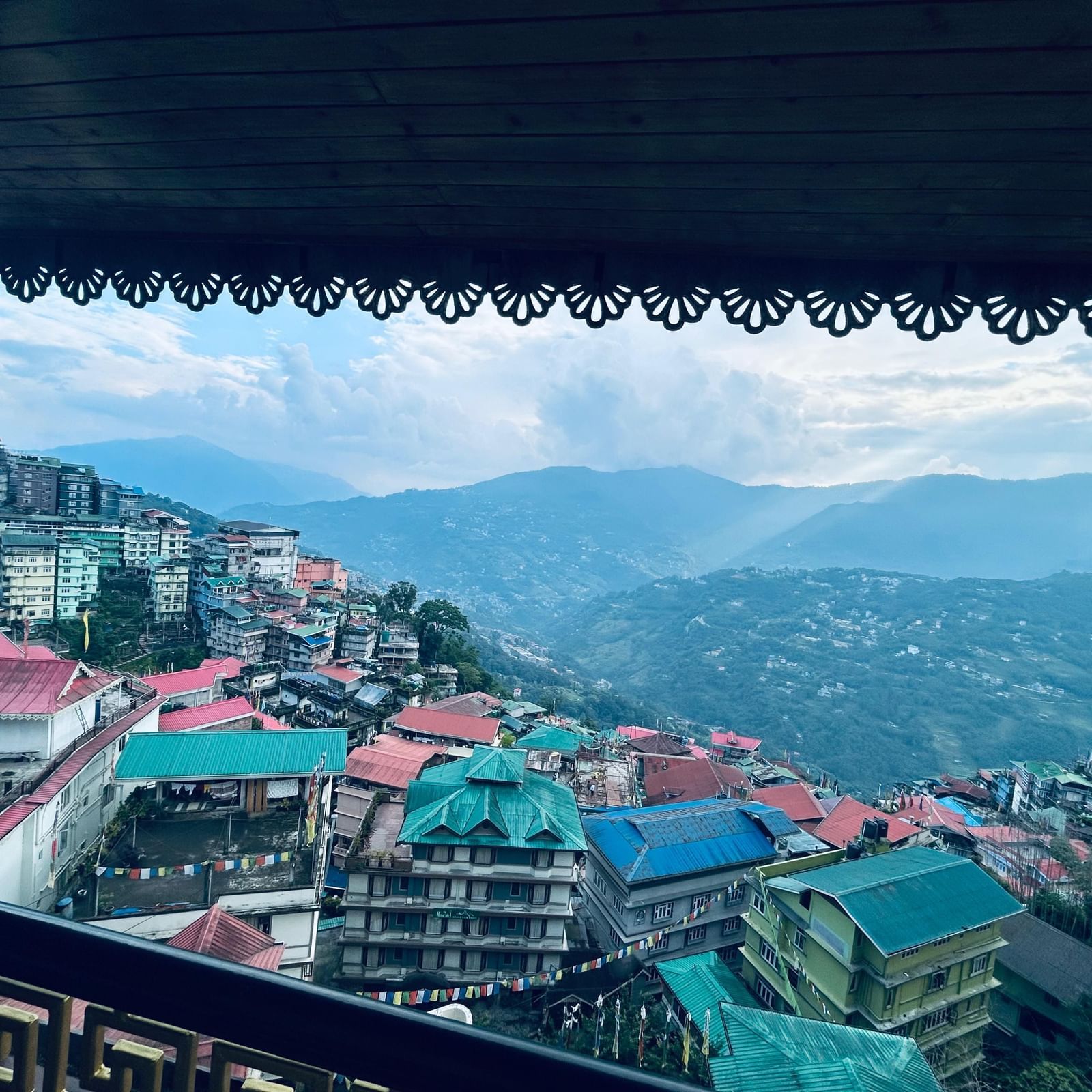 Colorful hillside houses and buildings in Gangtok city with mountains in the background under a cloudy sky.