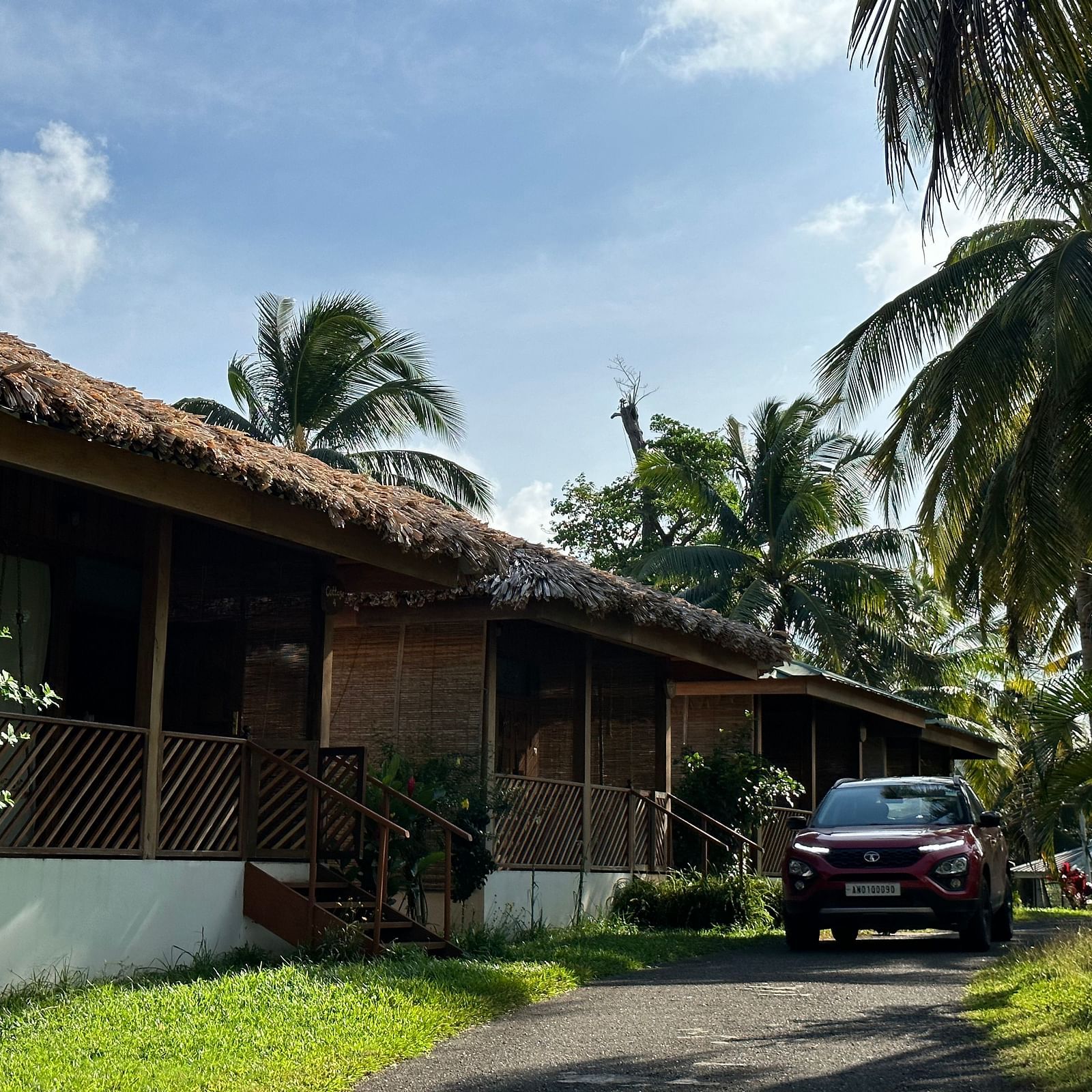 A charming resort building with a thatched roof, surrounded by lush green grass and palm trees under a bright sky.
