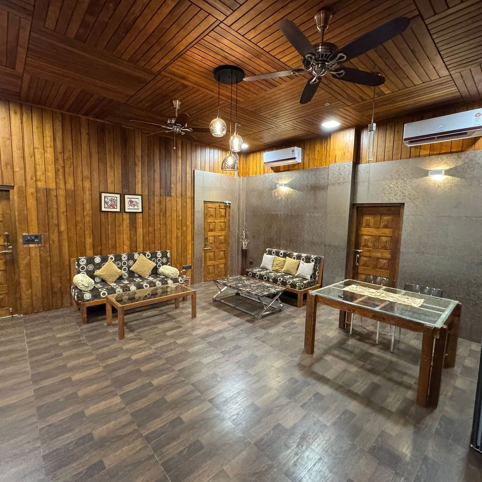 A wide-angle view of a rustic living area with wooden walls and ceiling, a patterned sofa, and a wooden coffee table.